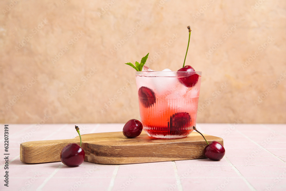 Wooden board with glass of tasty cherry lemonade and mint on pink tile table