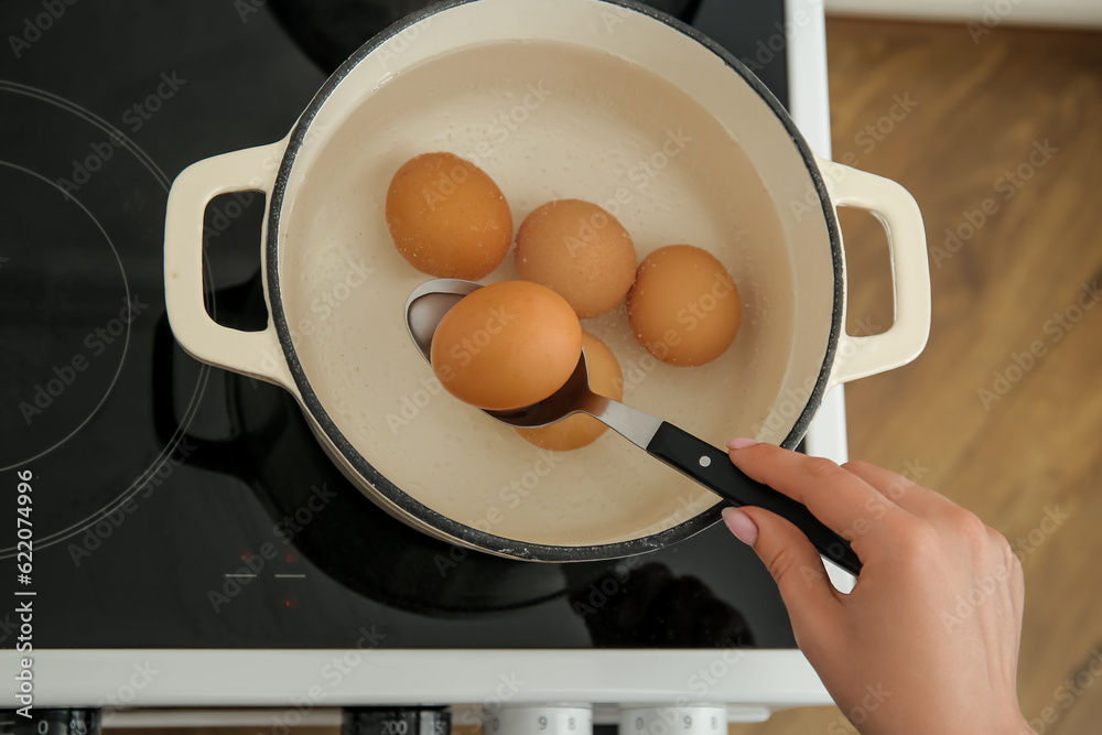 Woman taking chicken eggs from cooking pot on stove