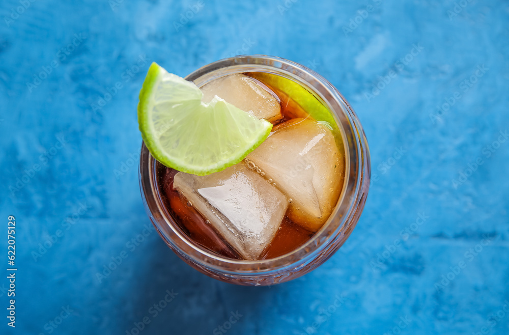 Glass of cold Cuba Libre cocktail on blue background