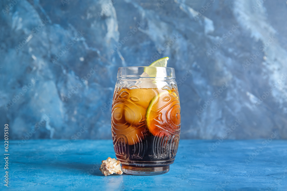 Glass of cold Cuba Libre cocktail and seashell on blue background