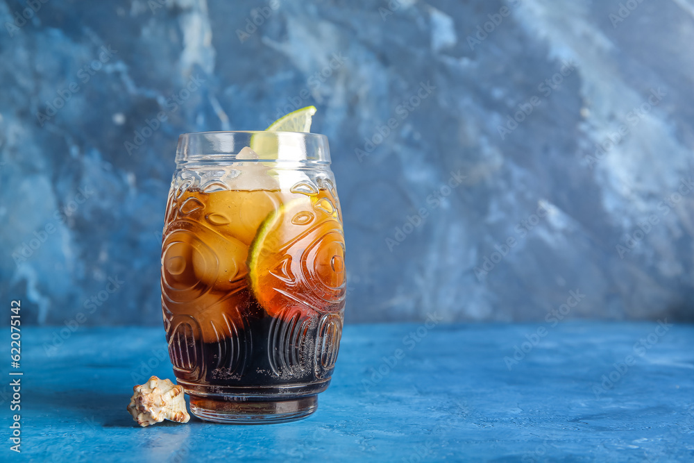 Glass of cold Cuba Libre cocktail and seashell on blue background