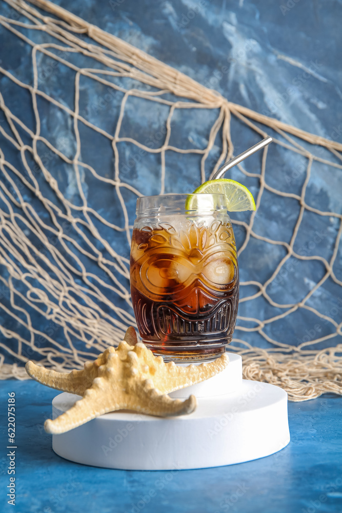 Decorative podium with glass of cold Cuba Libre cocktail and starfish on blue background