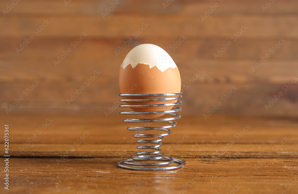 Holder with boiled chicken egg on wooden background