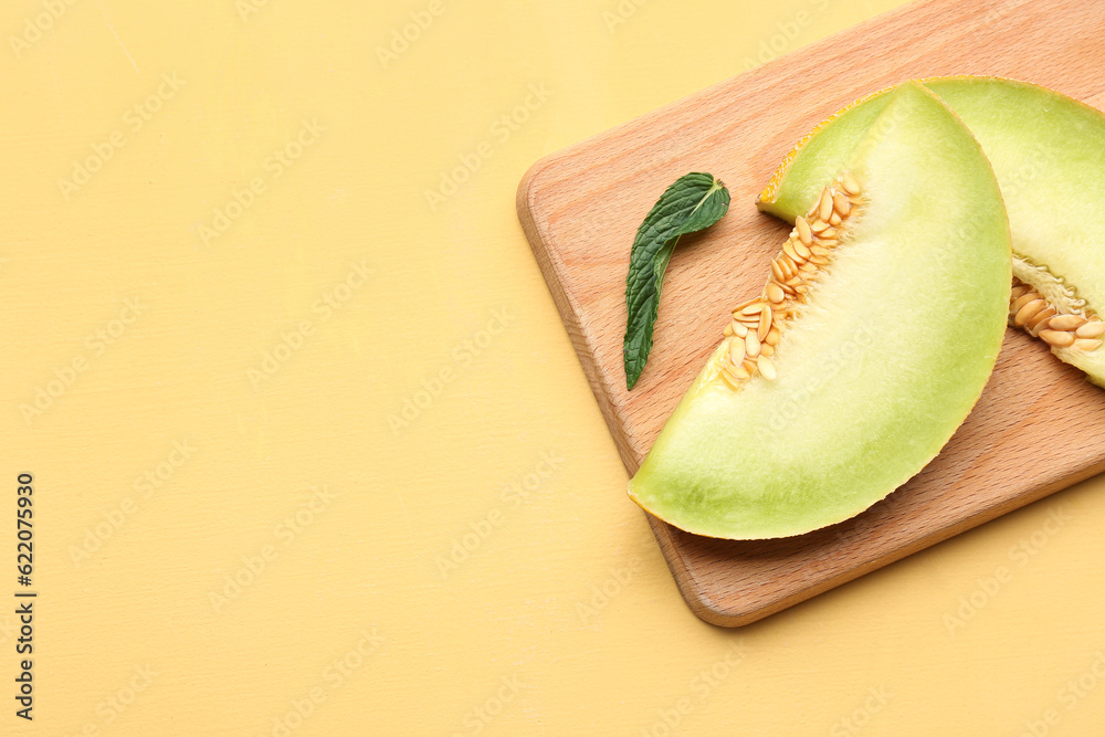 Wooden board with pieces of sweet melon and mint on yellow background