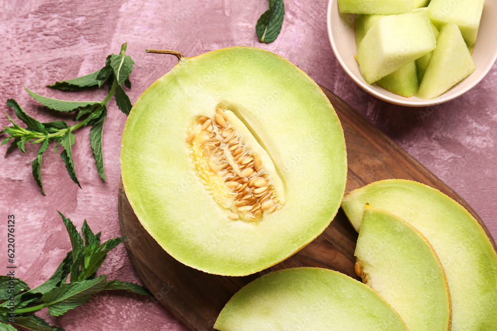 Wooden board with half of sweet melon and pieces on purple background