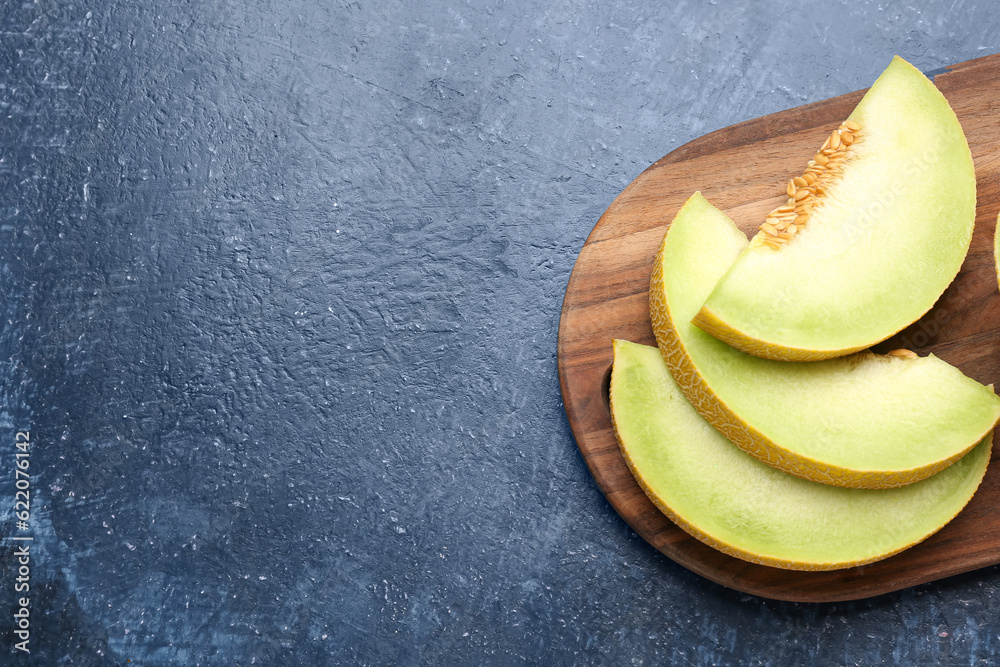 Wooden board with pieces of sweet melon on blue background