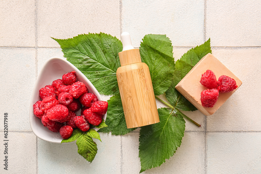 Bottle of cosmetic raspberry oil and bowl with berries on white tile background