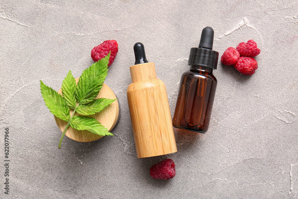 Bottles of cosmetic raspberry oil and jar with cream on grey background