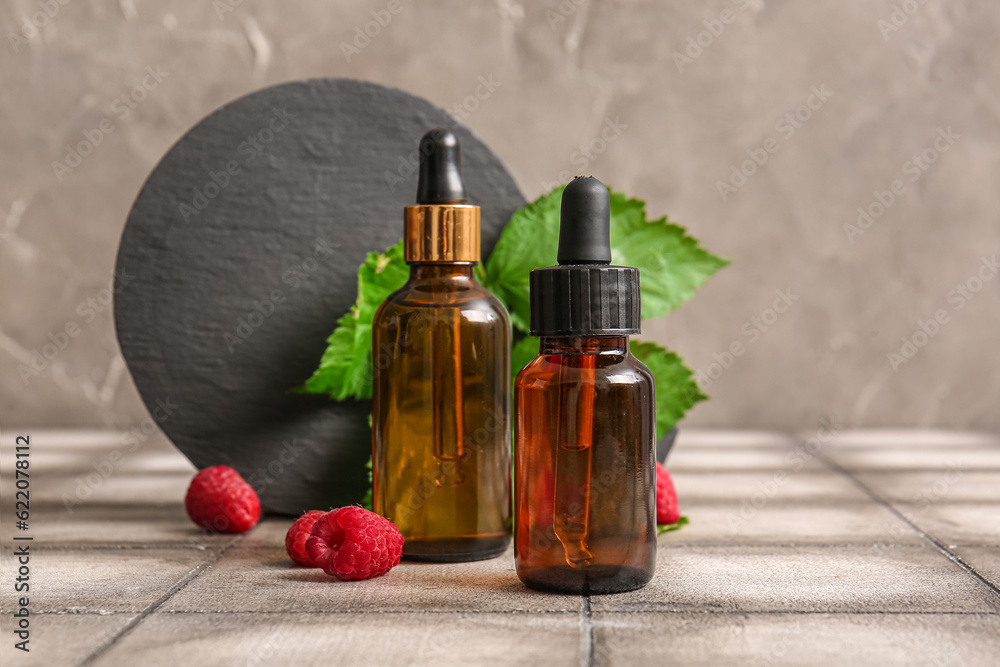 Bottles of cosmetic raspberry oil on grey tile table