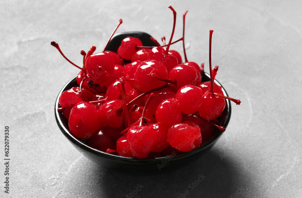 Bowl of tasty maraschino cherries on grey background