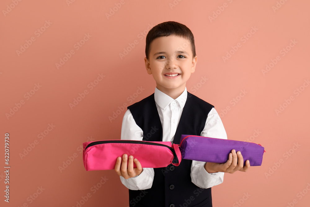 Cute little schoolboy with pencil cases on color background