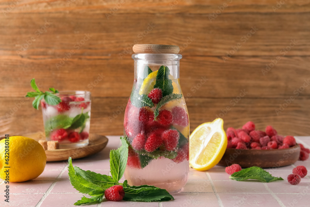 Bottle and glass of fresh raspberry lemonade with mint on pink tile table