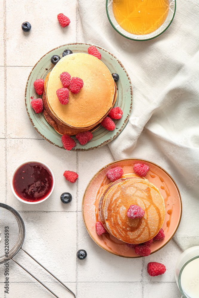 Plates of tasty pancakes with raspberries and blueberries on white tile background