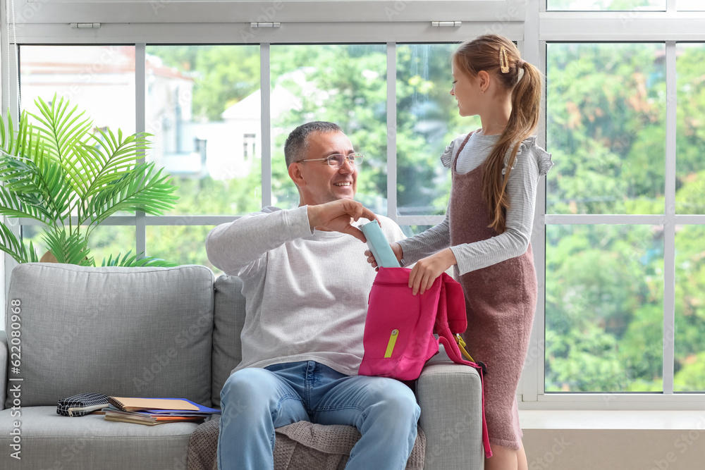 Father helping his little daughter to pack schoolbag in kitchen