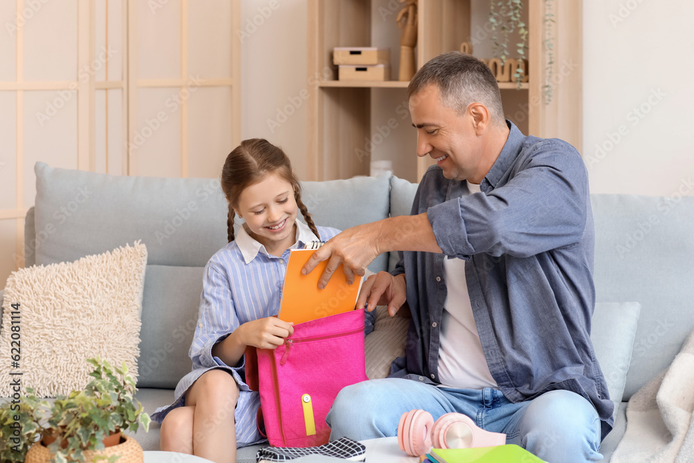 Father helping his little daughter to pack schoolbag at home