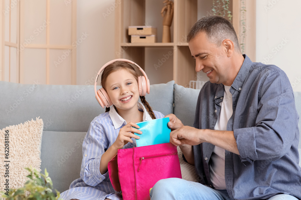 Father helping his little daughter to pack schoolbag at home