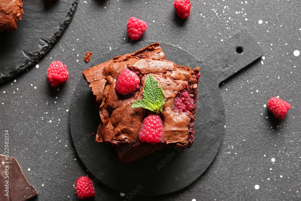 Board with pieces of raspberry chocolate brownie on black table