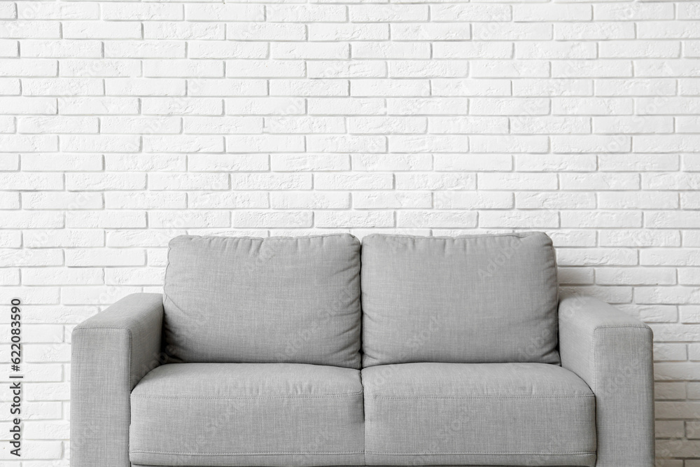 Cozy grey sofa near white brick wall