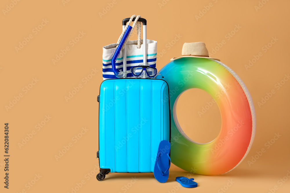 Suitcase with inflatable ring and beach accessories on beige background. Travel concept