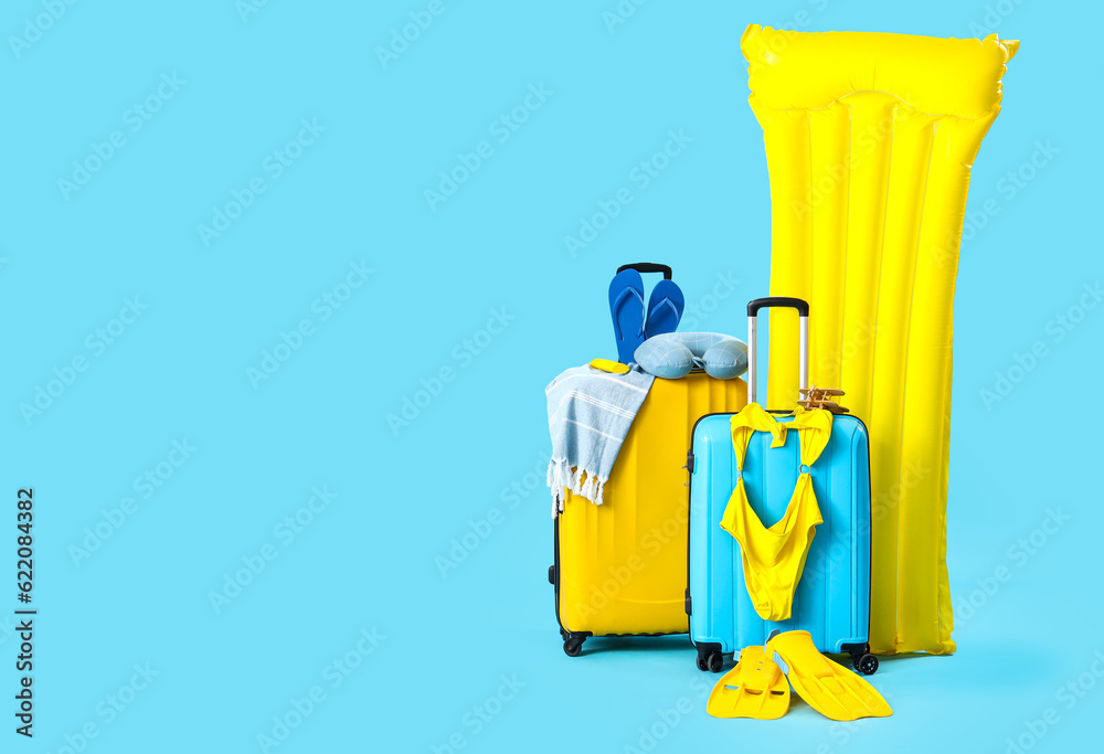 Suitcases with inflatable mattress and different beach accessories on blue background. Travel concep