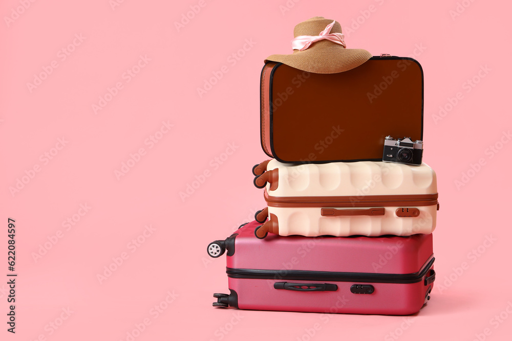 Suitcases with wicker hat and camera on pink background. Travel concept