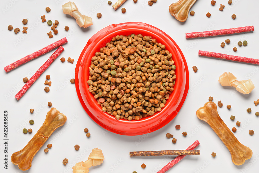 Composition with bowl of dry dog food and different treats on light background