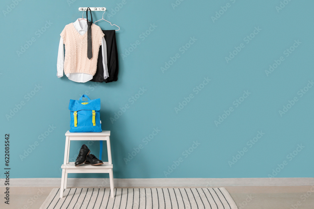 Step ladder with school backpack, shoes and uniform hanging on color wall