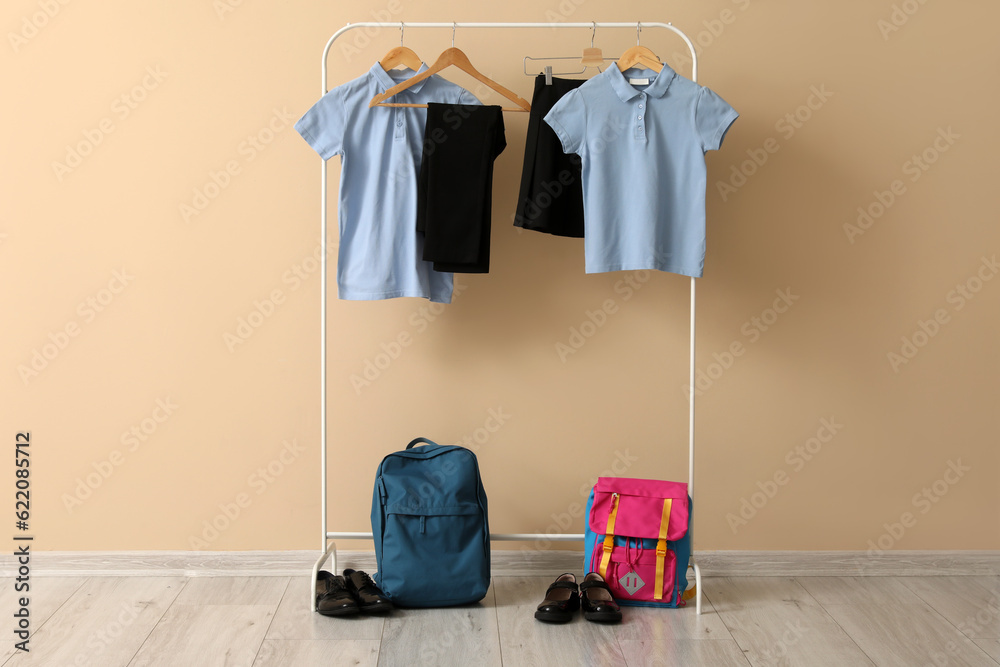 Rack with stylish school uniform, backpacks and shoes near color wall