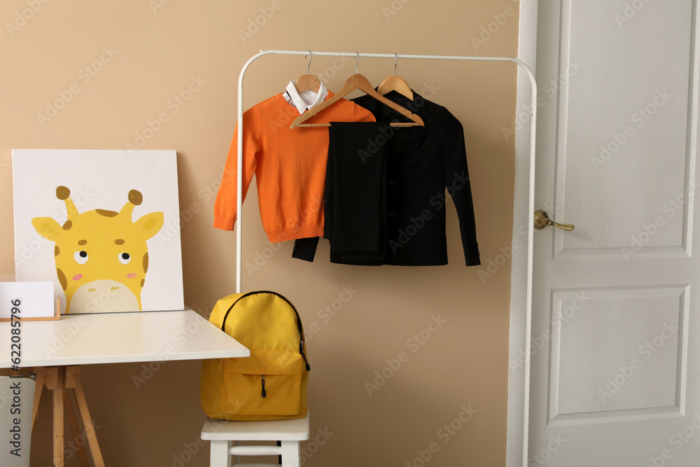 Rack with stylish school uniform and backpack near color wall in childrens room