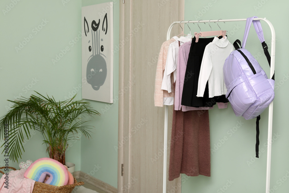 Stylish school uniform and backpack hanging on rack in childrens room