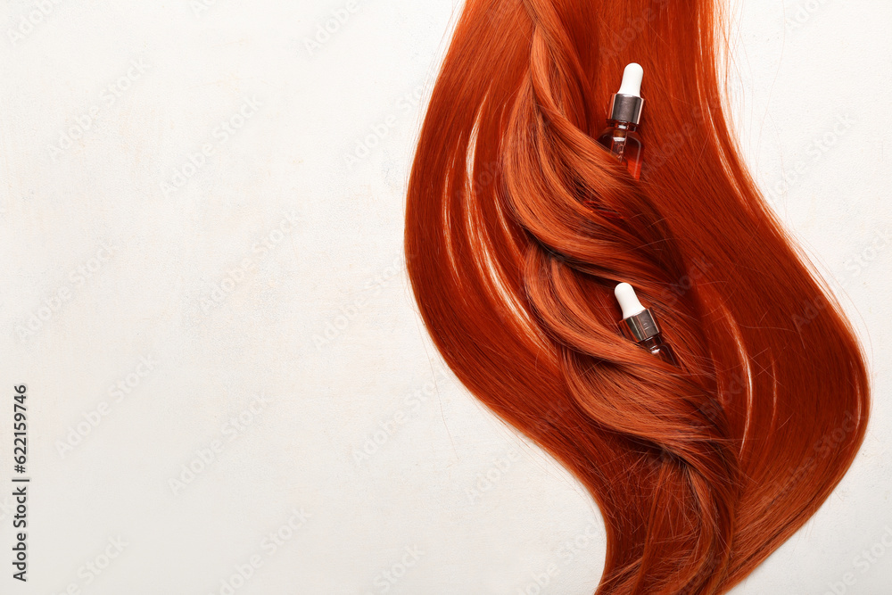 Beautiful ginger hair with bottles of essential oil on light background, closeup