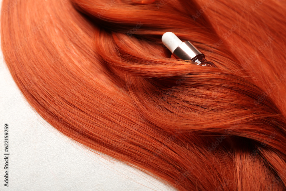 Beautiful ginger hair with bottle of essential oil on light background, closeup