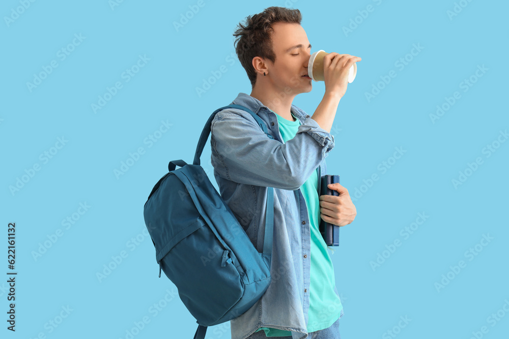 Male student with backpack and books drinking coffee on blue background