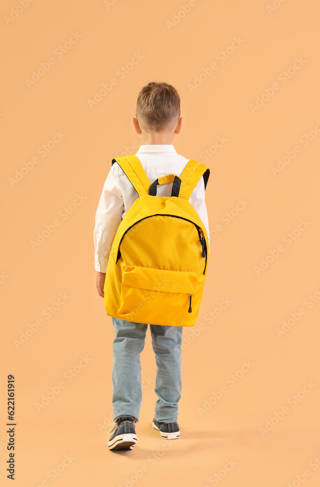 Little schoolboy with yellow backpack on orange background, back view