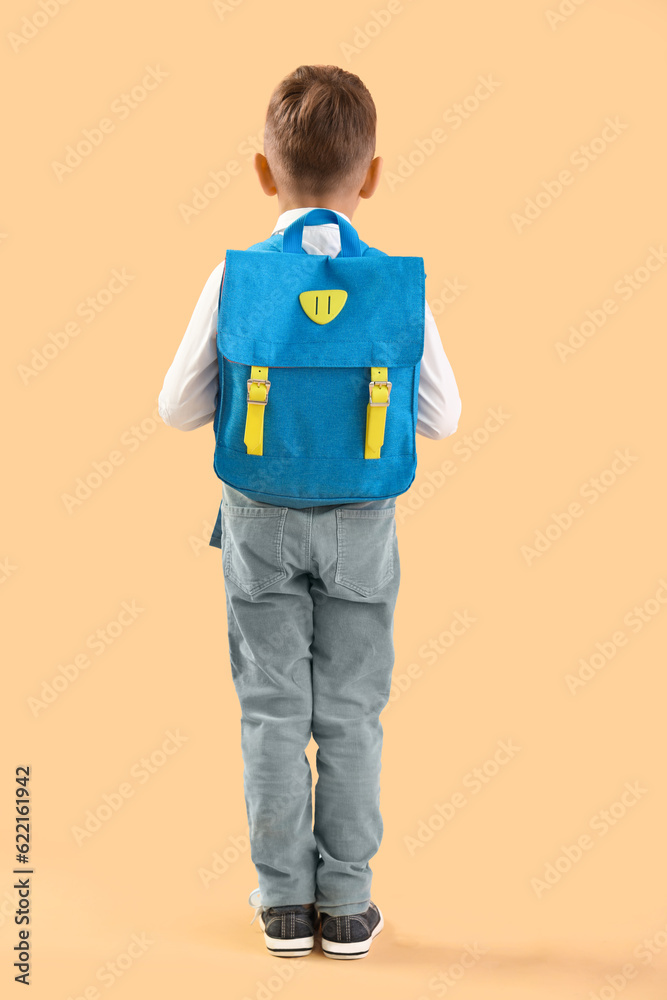 Little schoolboy with blue backpack on orange background, back view