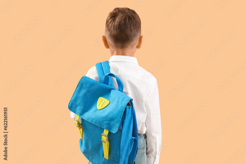 Little schoolboy with blue backpack on orange background, back view