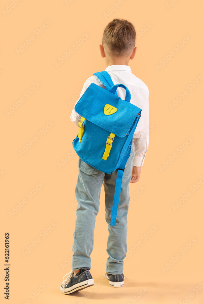 Little schoolboy with blue backpack on orange background, back view