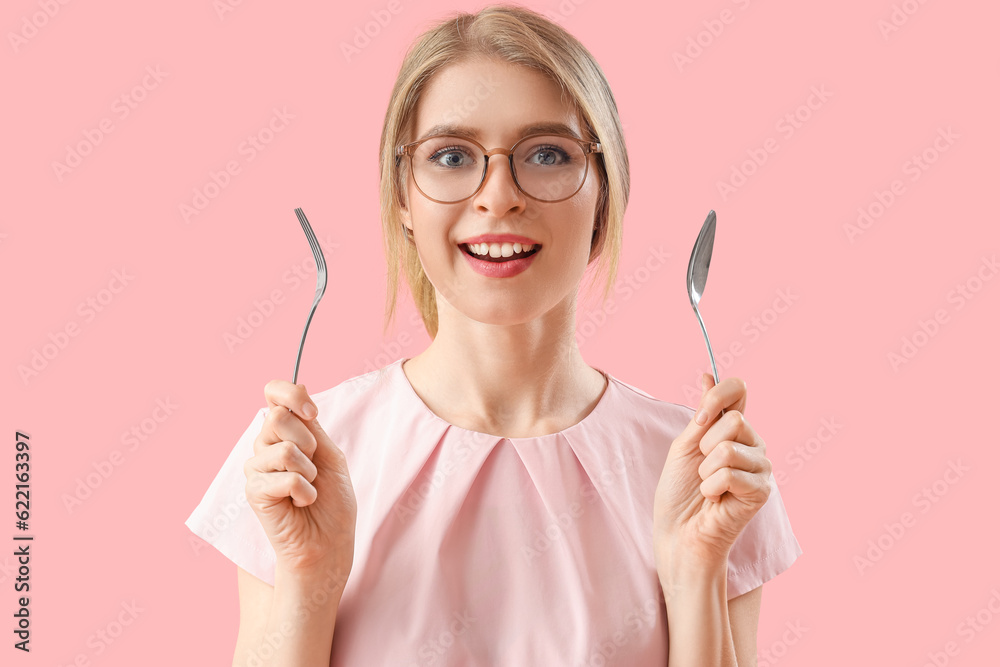 Young woman with spoon and fork on pink background