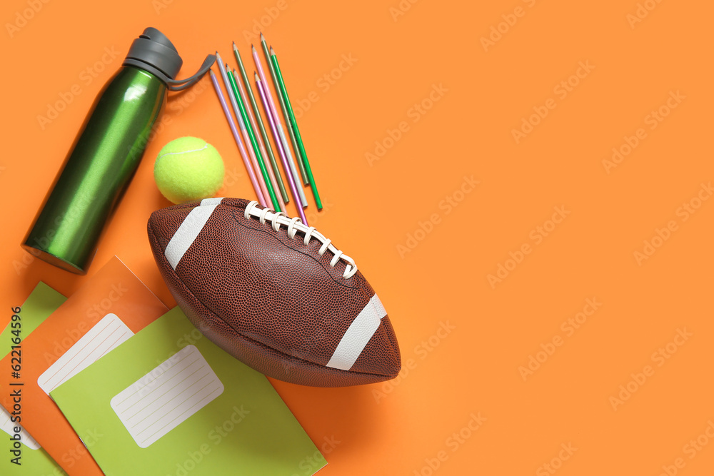 Bottle of water with different stationery, rugby and tennis balls on orange background