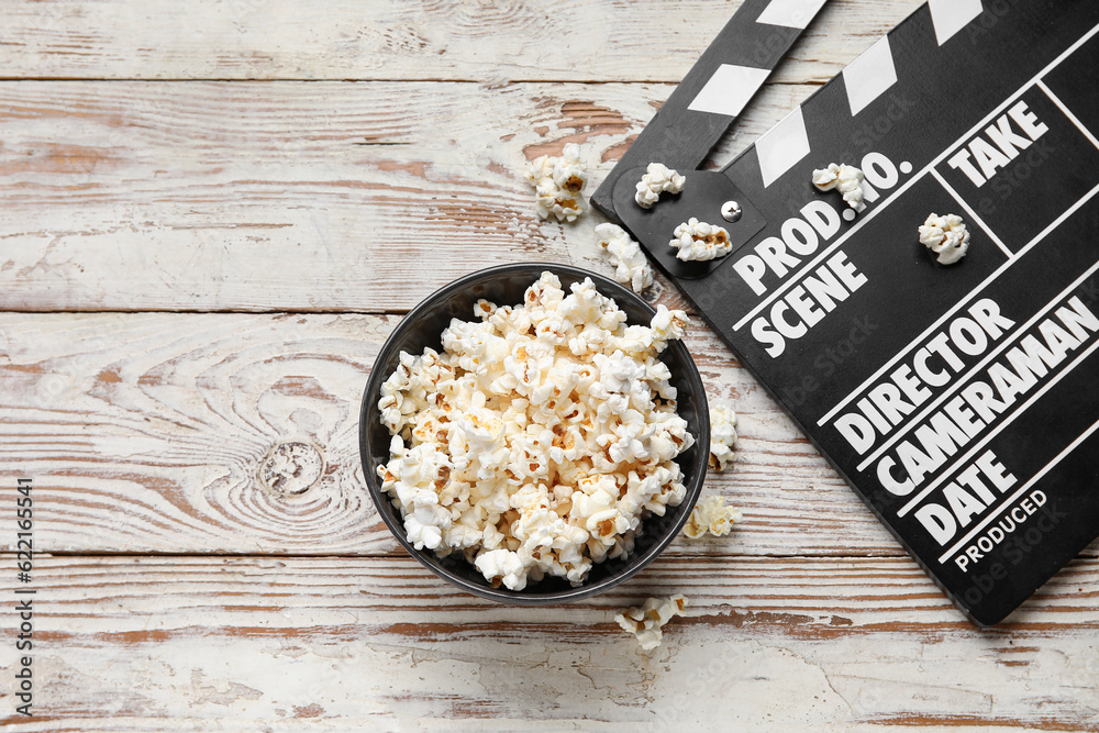 Bowl with tasty popcorn and clapperboard on white wooden background