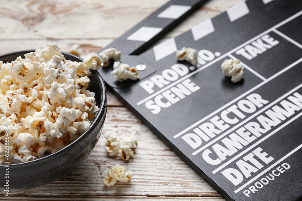 Bowl with tasty popcorn and clapperboard on white wooden background