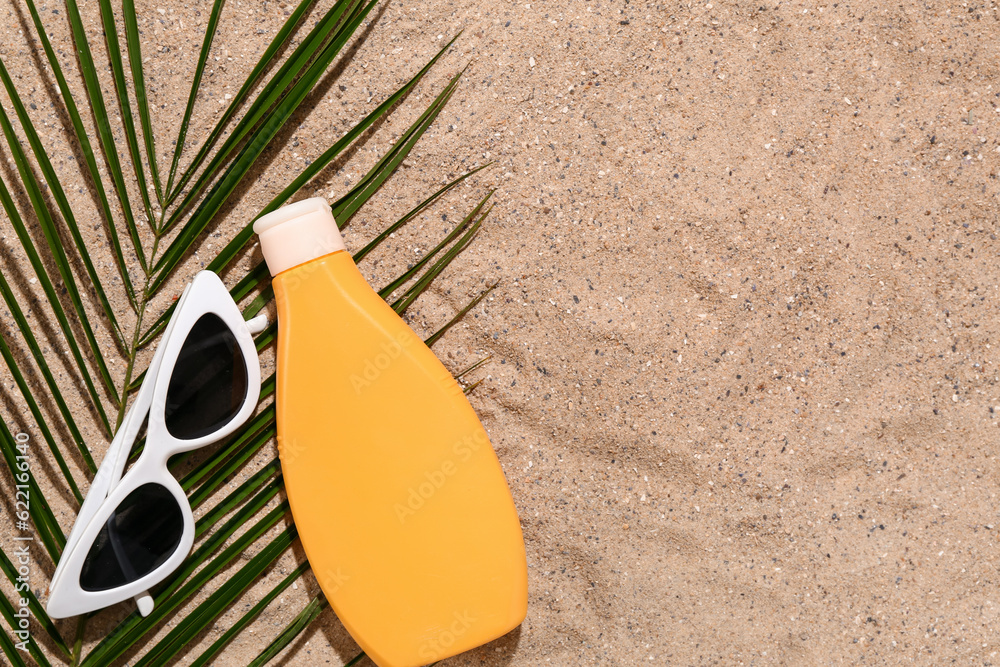 Sunglasses with bottle of sunscreen cream and palm leaf on sand