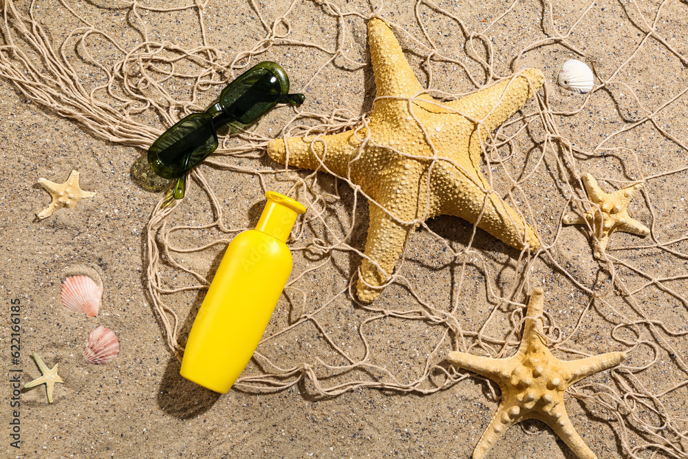 Sunglasses with starfishes, seashells and bottle of sunscreen cream on sand