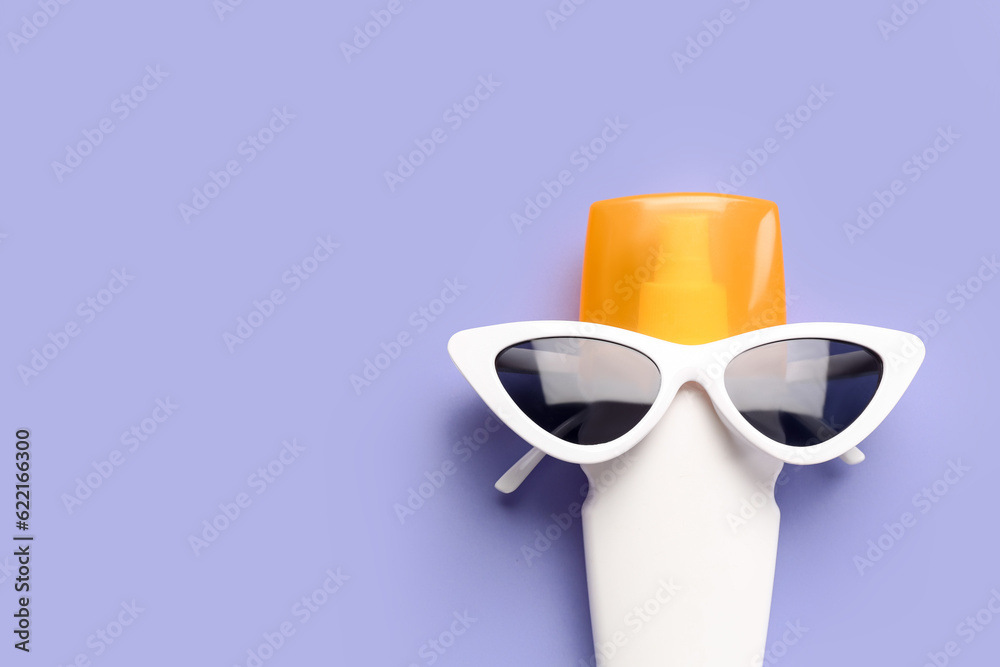 Creative composition with sunglasses and bottle of sunscreen cream on lilac background