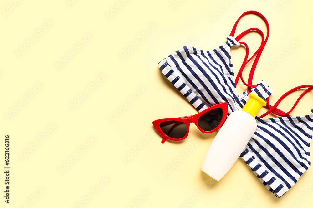 Sunglasses with bikini bra and bottle of sunscreen cream on pale yellow background