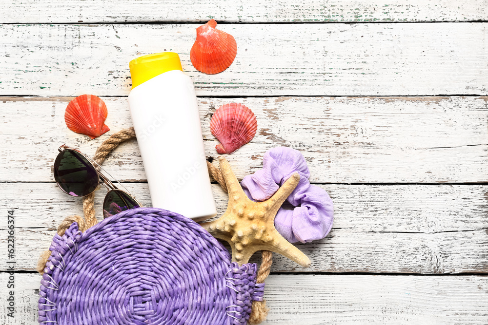 Wicker bag with sunglasses, hair band and bottle of sunscreen cream on white wooden background