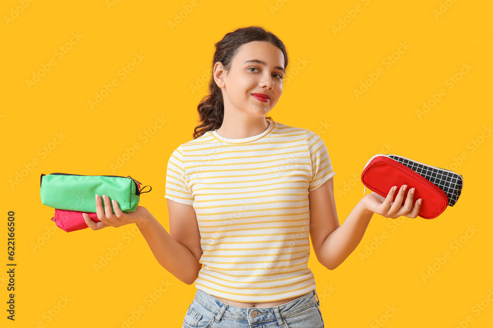 Female student with pencil cases on yellow background