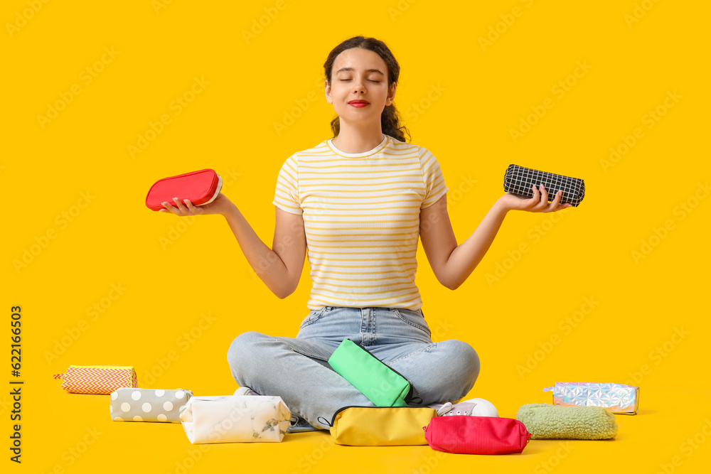 Female student with pencil cases sitting on yellow background