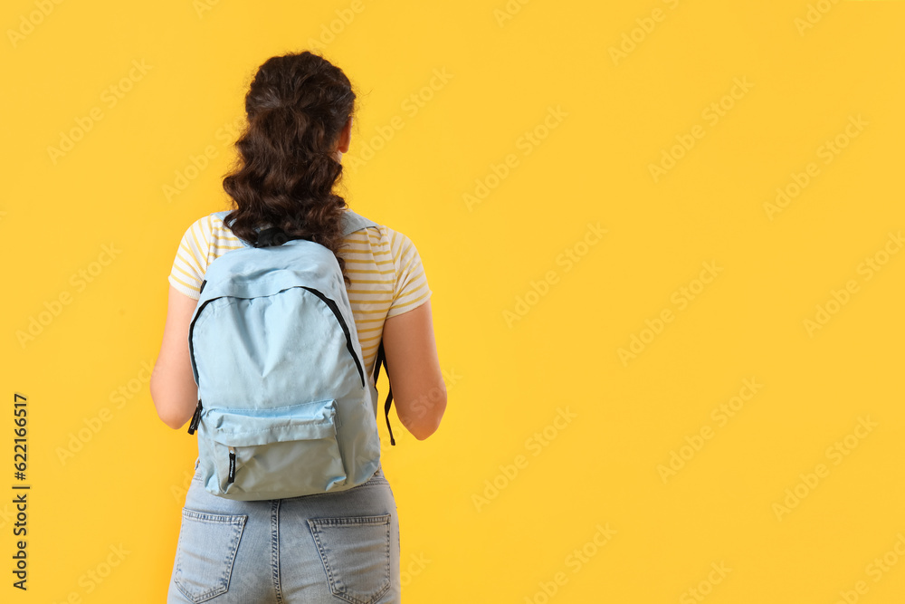 Female student with backpack on yellow background, back view