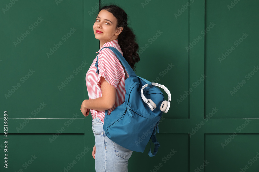 Female student with backpack near green wall